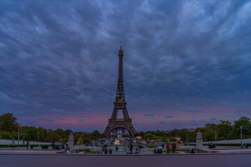 Fototapeta na wymiar Purple Sky at Evening Over Eiffel Tower With Tourists Denses Clouds and Trees