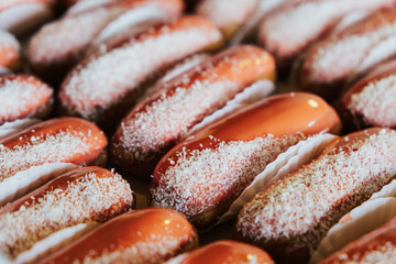 Close up of eclairs with chocolate topping and coconut flakes. éclair is a pastry made with choux dough filled with a cream and topped with a flavored icing. 