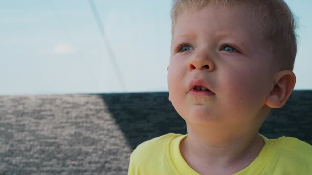 Cute toddler child boy with chubby cheeks in yellow t-shirt yawns in gondola riding cable way at mountain resort close view slow motion