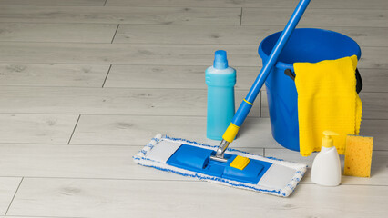 Blue cleaning accessories and a yellow rag on the wooden floor. The concept of maintaining...