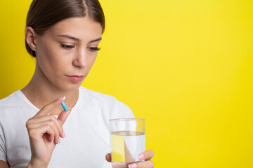 Unhappy woman holds pill and glass of water