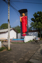 Fototapeta na wymiar Ella, Sri Lanka A red Buddhah statue stands by the side of the road.
