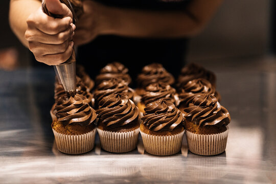 Female baker squeezing cream on muffins