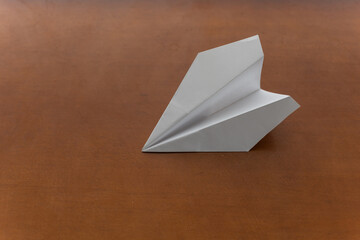 Flat lay of white paper plane on pastel brown background.