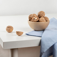 There is a wooden bowl with walnuts on a white table, and a blue towel is lying next to it. Close-up.