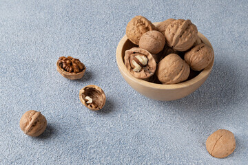 Wooden bowl with walnuts in the shell. Blue textured background, close-up, horizontal orientation.