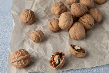 A scattering of walnuts in a shell on parchment paper. Close-up, horizontal orientation.