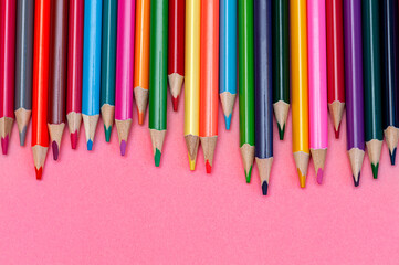 Border of colored pencils on pink background, copy space