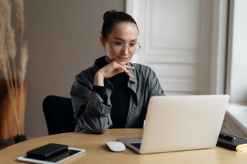 Fototapeta premium The manager is a woman with glasses working in the office using a laptop computer online project report
