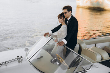 Groom in a black suit and sunglasses hugs the bride on a yacht. Wedding day