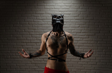 a man with a naked torso in a bdsm demon mask with tattoos and leather belts and handcuffs