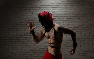 a man with a naked torso in a bdsm demon mask with tattoos and leather belts and handcuffs