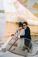 Man in a black suit and sunglasses hugs a woman on a yacht on a sunny day. Bride and groom.