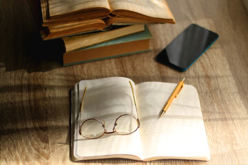 Open book, mechanical pencil, reading glasses, mobile phone and strack of books on the desk....