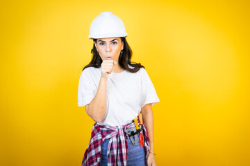 Young caucasian woman wearing hardhat and builder clothes over isolated yellow background with her hand to her mouth because she's coughing