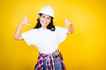 Young caucasian woman wearing hardhat and builder clothes over isolated yellow background shouting...