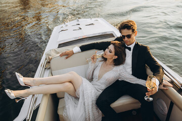 Stylish young bride and groom huging and kissing on yacht - obrazy, fototapety, plakaty