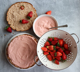 Strawberry cream, cake layers and juicy strawberries on a table. Close up photo of homemade cake in process. Layer cake ingredients top view. 