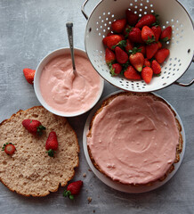 Strawberry cream, cake layers and juicy strawberries on a table. Close up photo of homemade cake in process. Layer cake ingredients top view. 