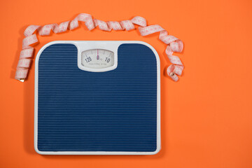 Floor blue scales and centimeter measuring tape on an orange background, top view. The concept of...