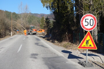 Workers with payloader and truck with hydraulic lifting platform remove a tree fallen on the road....