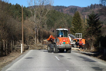 Fototapeta na wymiar Workers with payloader and truck with hydraulic lifting platform remove a tree fallen on the road. highway work concept