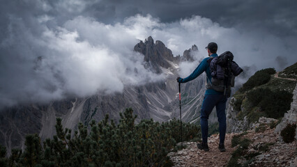 Man hiking with view to mountain peaks in the Dolomite Alps in South Tyrol with dramatic cloudy sky, Three Peaks Nature Reserve, Italy.