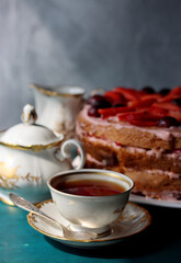 Vintage cup with black tea, strawberry cake and fresh berries on textured background. Sweet food still life. Birthday cake close up photo. 