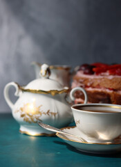Retro tableware on a table. Cup of tea, milk jug, fresh berries and strawberry cake. Textured background with copy space. 