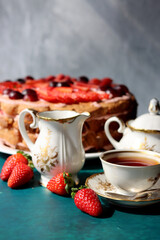 Retro tea party. Beautiful white and gold cup, sugar bowl, milk jug and strawberry cake. Sunny morning photo. Sweet food on a table. 