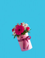 Pink gift box with various spring flowers on blue background. Mother's Day idea. Copy space.