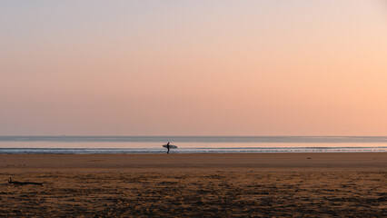 Fototapeta na wymiar The pastel pinks and blues glow above a lone surfer at the water's edge on Belhaven Bay to the south of the North Sea