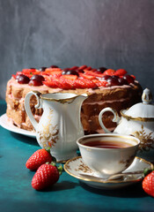 Retro tableware on a table. Cup of tea, milk jug, fresh berries and strawberry cake. Textured background with copy space. 