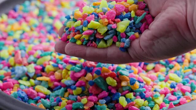 hand pouring crushed colored stones on flat surface with slo-mo