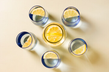 vasos con agua y limón haciendo círculo con jarra en el centro, fondo amarilllo pastel