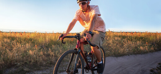 Fototapeta na wymiar Cyclist on a gravel bike riding a trail in a field on a dramatic sunset background.