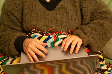 manos en el ordenador con el sofá con manta de lana colorida vintage