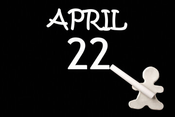 A small white plasticine man writing the date 22 April on a black board. Business concept. Education concept.
