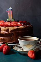First Birthday's cake on a table. Close up photo of strawberry cake, fresh juicy berries and cup of tea. Beautiful homemade dessert photo.  