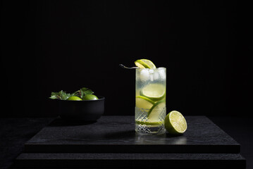 Un vaso de refrescante cóctel de jugo de lima con rodajas de lima y hielo sobre fondo negro	