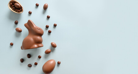 Happy Easter greeting card with chocolate sweets rabbit, eggs on blue background. Concept egg hunt.