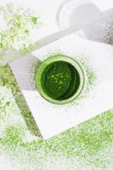 Un vaso de té matcha con polvo de té verde espolvoreado sobre una mesa blanca. Vista superior	
