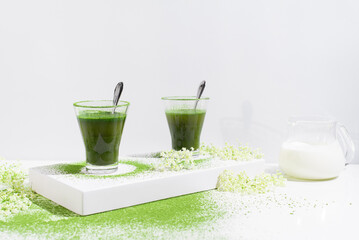 Dos vasos de té matcha con polvo de té verde espolvoreado sobre una mesa blanca	