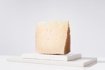 Trozo de queso curado manchego de oveja sobre mesa blanca y fondo claro. Aperitivo español