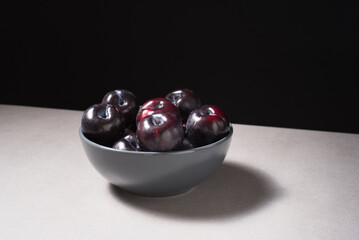 Ciruelas negras maduras en un plato gris sobre fondo negro