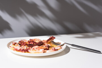 Plato de pulpo a la gallega con pimentón y aceite de oliva. Tapa típica española sobre mesa blanca