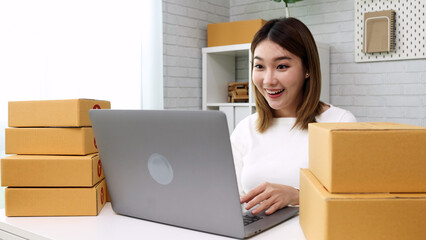 Happy young Asian woman using laptop computer and checking product order, Small online business owner concept