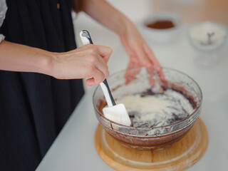 DIY home cooking concept. brunette woman sifting flour for cake through sieve, salting dough. Young woman smiling, loves to cook in beautiful modern kitchen.