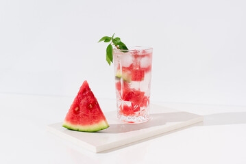 Un vaso de zumo de sandía con trozos de sandia y hielo sobre fondo claro	