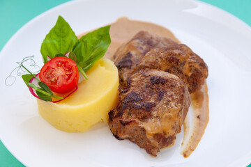 Beef cutlets meatballs with mashed potatoes on a white plate. Meat in sour cream sauce. Tomatoes and basil. Food in the restaurant. Lunch portion. Medallions.
